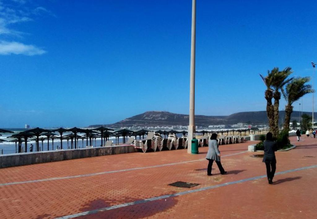 Boulevard langs het strand in Agadir met palmbomen, ligbedden en uitzicht op de baai.