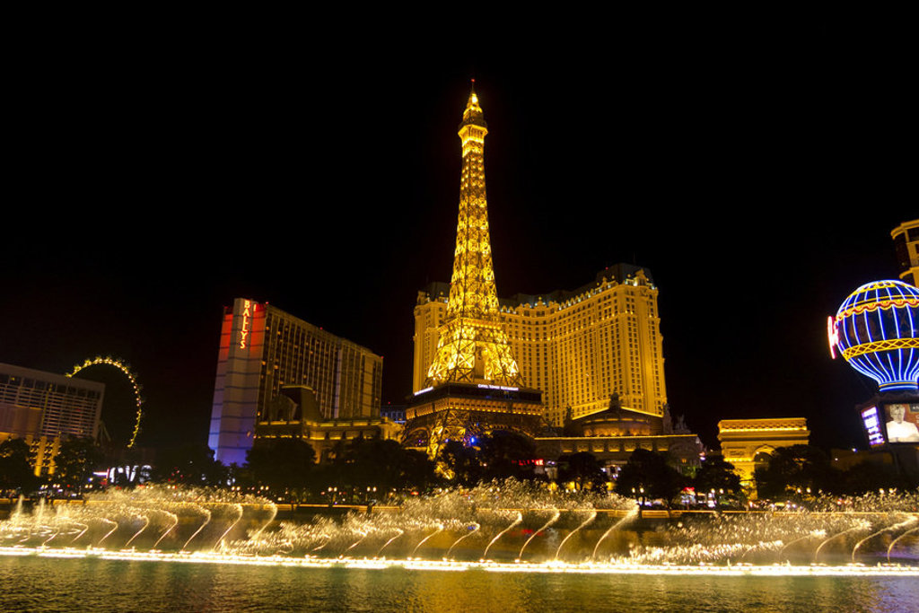 Nachtzicht op de verlichte Eiffeltoren bij hotel Paris Las Vegas met fonteinshow op de Strip.