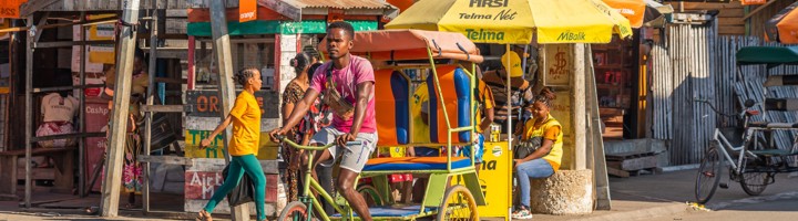 Fietstaxi op straat in Morondava, Madagascar, met kleurrijke marktkraampjes op de achtergrond.