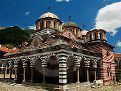 Rila-klooster in Bulgarije met gestreepte bogen en koepels onder een blauwe lucht.