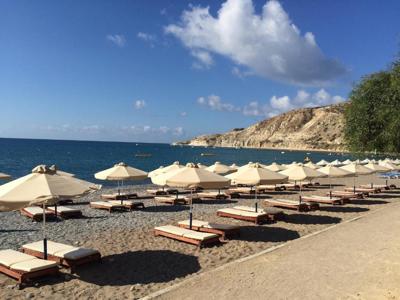 Strand op Cyprus met ligbedden en parasols aan een baai met rotsachtige kust en helderblauwe zee.