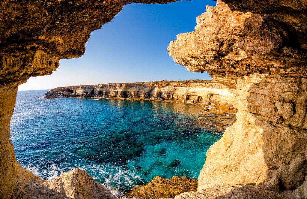 Rotsachtige kust en zeegrotten aan helderblauw water op Cyprus, gezien vanuit een grot.