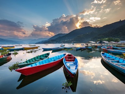 Gekleurde roeiboten op Phewa Lake bij Pokhara, met bergen en zonsondergang in Nepal.