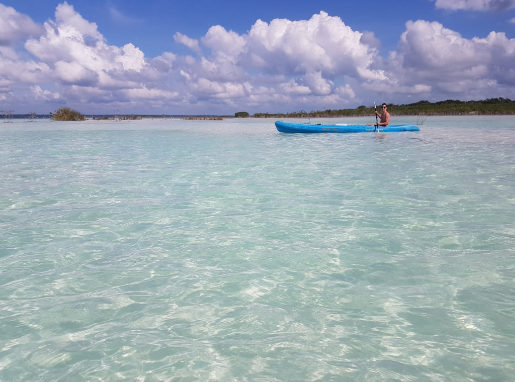 Man in een blauwe kajak op helderblauw water in Mexico, tijdens een familiereis.