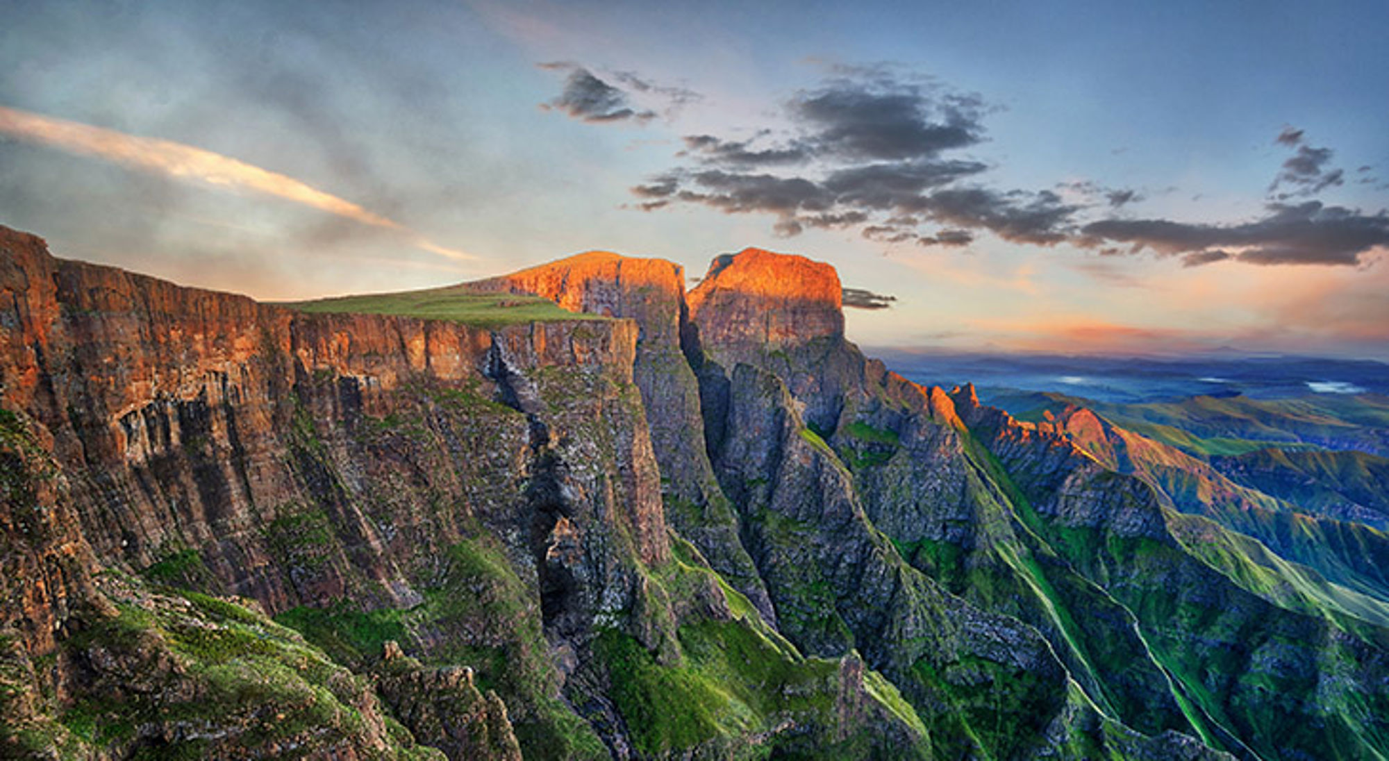 zuid-afrika-drakensbergen Zonsondergang boven ruige bergkliffen en groene valleien.