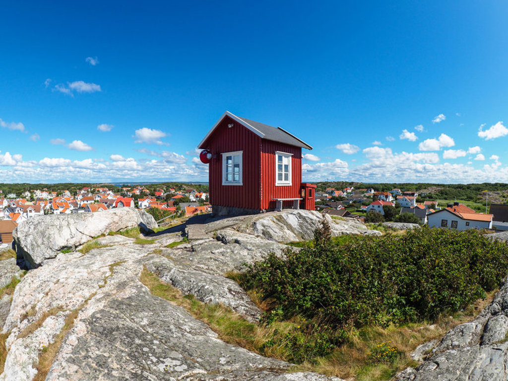 Rood houten huisje op rotsen met uitzicht over een kustplaats in Zweden tijdens een groepsrondreis Scandinavië.